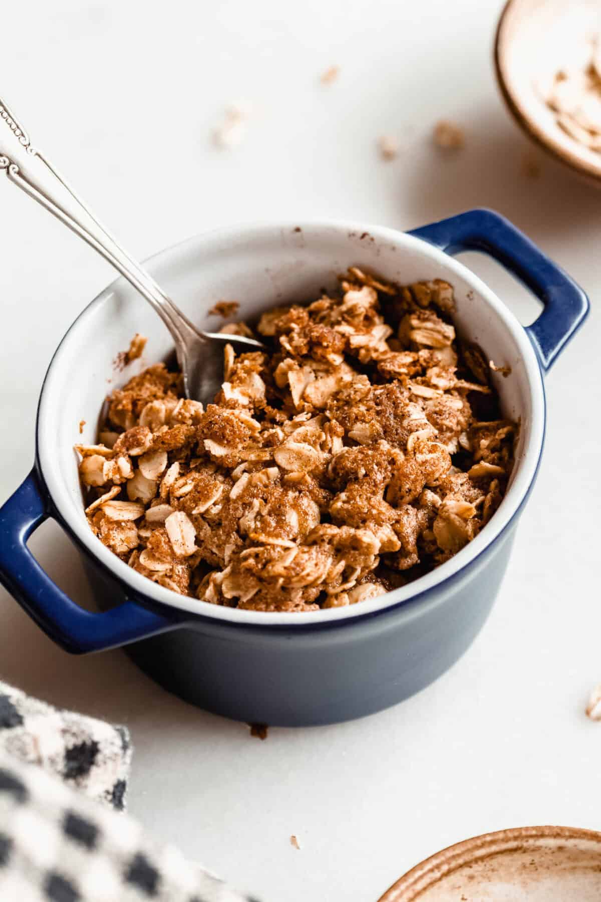 A spoon scooping into a baked apple crisp with a crispy golden brown oat topping.