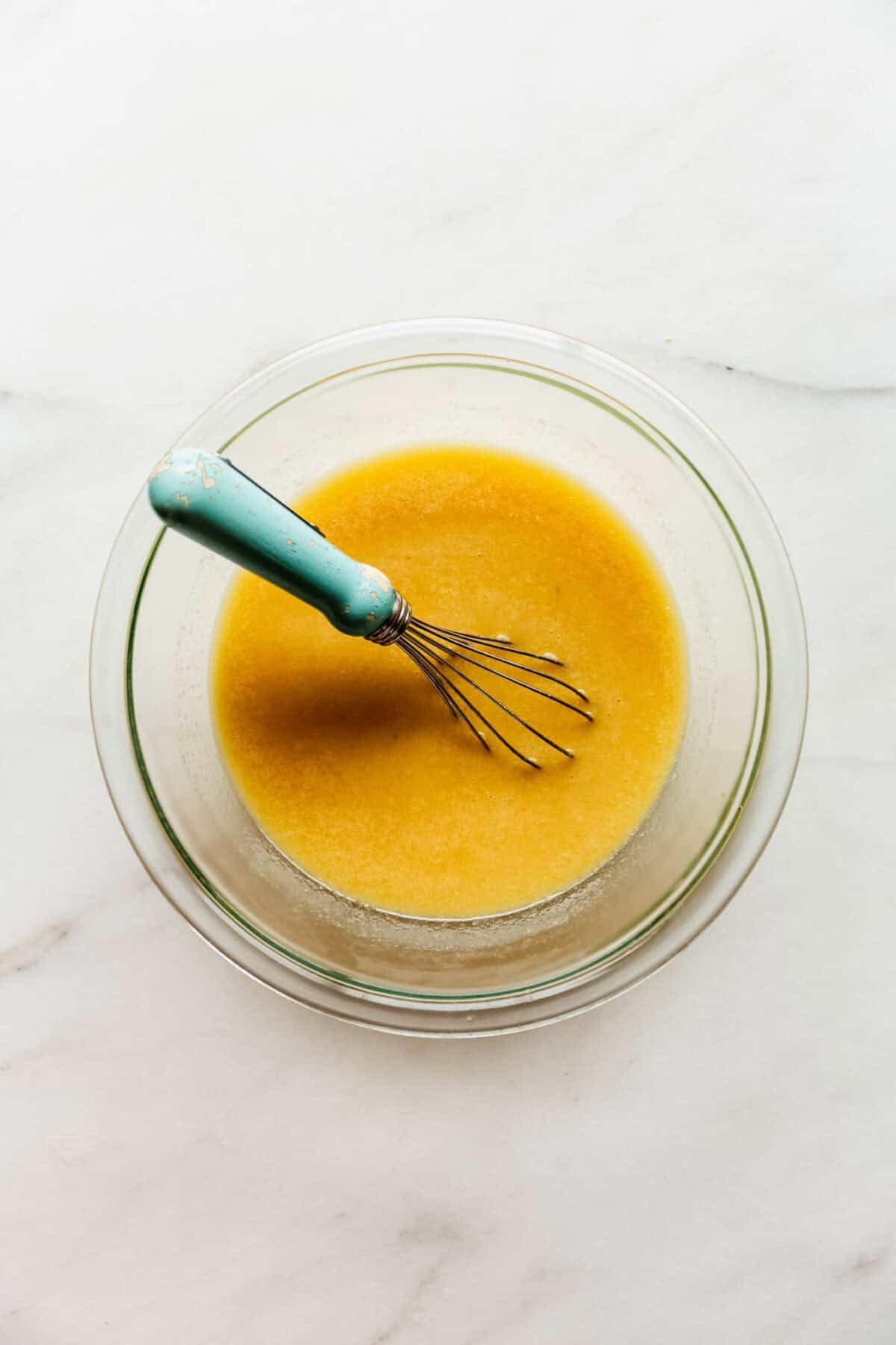 A whisk blending the wet batter ingredients together in a glass bowl.