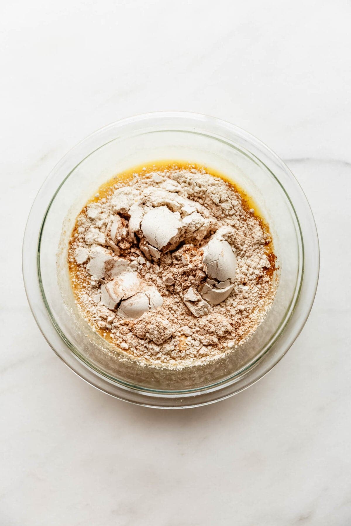 Dry flour and oat ingredients added on top of the wet mixture in a glass bowl before stirring.