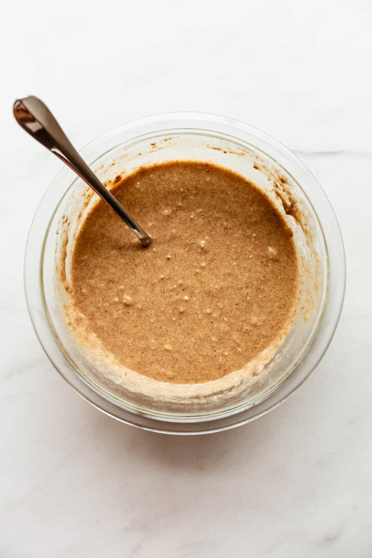 The combined oat batter in a glass jar with a spoon resting inside before portioning.