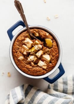A single-serving apple baked oatmeal in a small blue dish topped with fresh apple slices and a spoon.