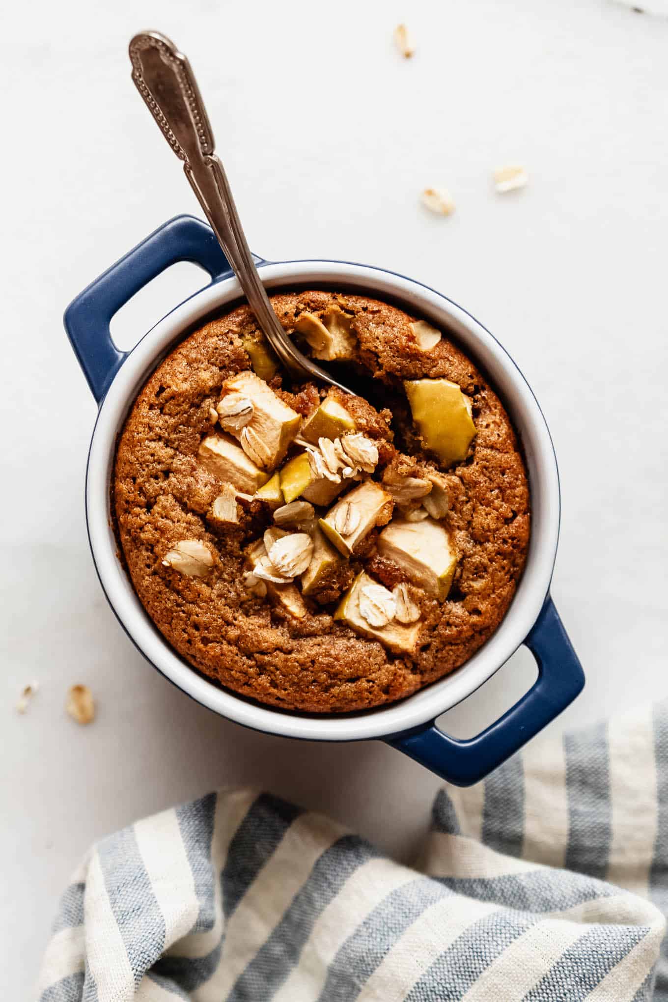 A single-serving apple baked oatmeal in a small blue dish topped with fresh apple slices and a spoon.