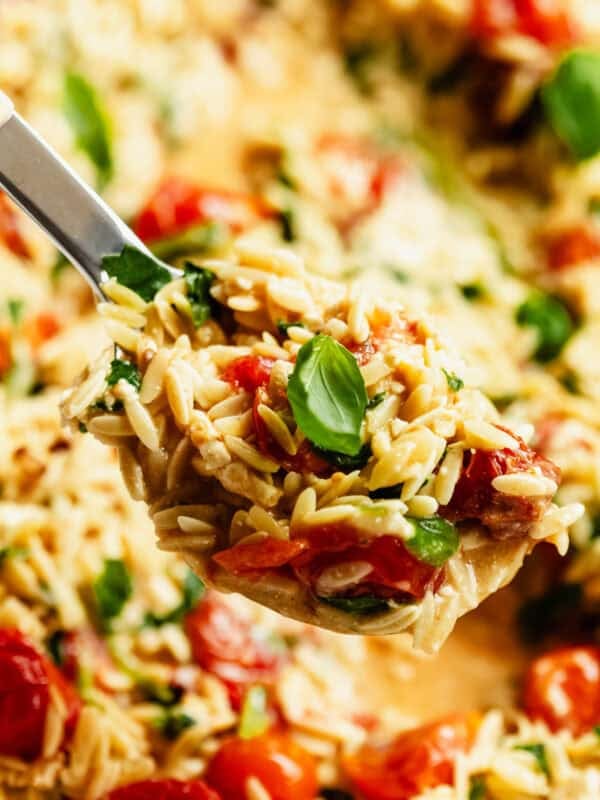 Fork lifting a bite of baked feta tomato orzo topped with fresh basil.