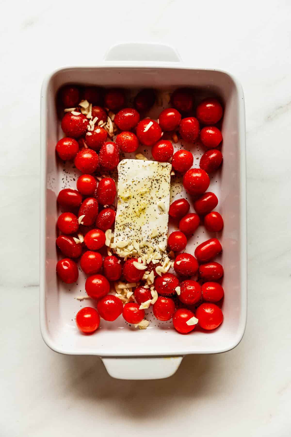 Unbaked dish of cherry tomatoes, garlic, and feta cheese ready for the oven.