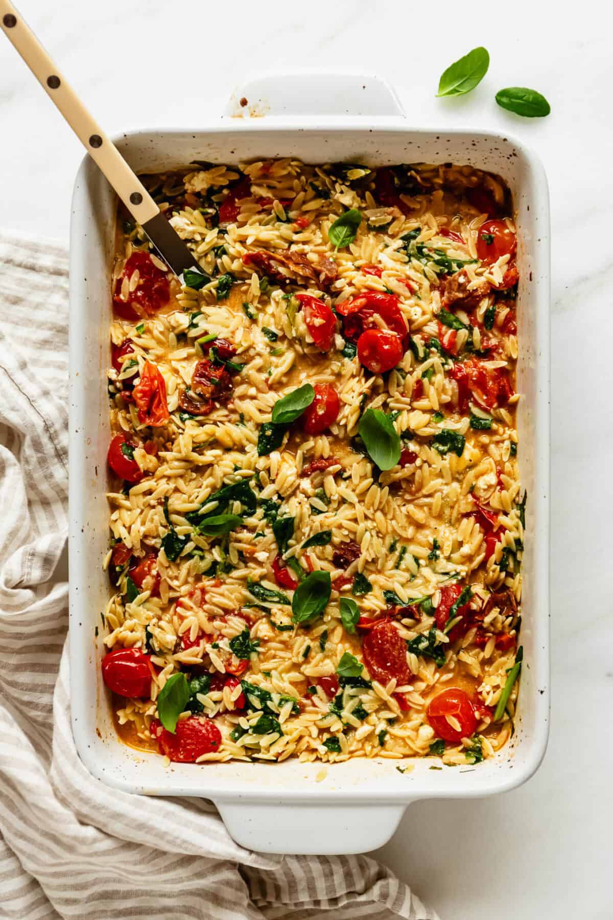 Baked feta tomato orzo garnished with fresh basil leaves in a white baking dish.