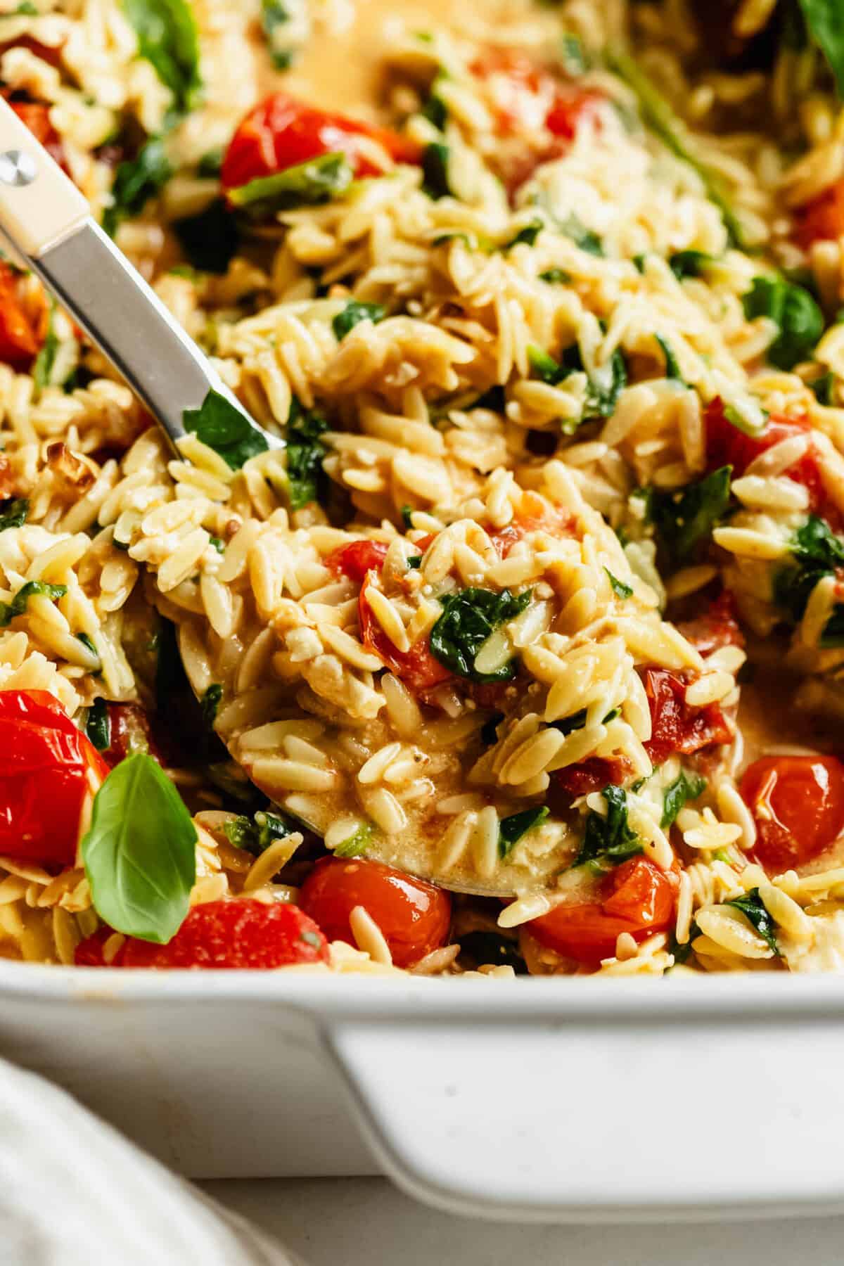 Close-up of a spoon scooping baked feta tomato orzo from the dish.