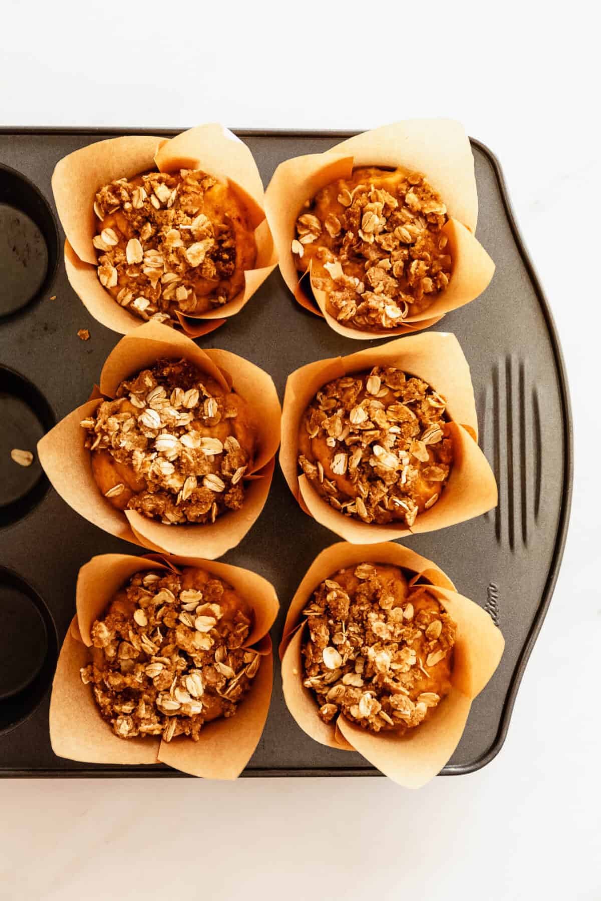 Muffin tin filled with unbaked banana pumpkin muffin batter topped with oats.
