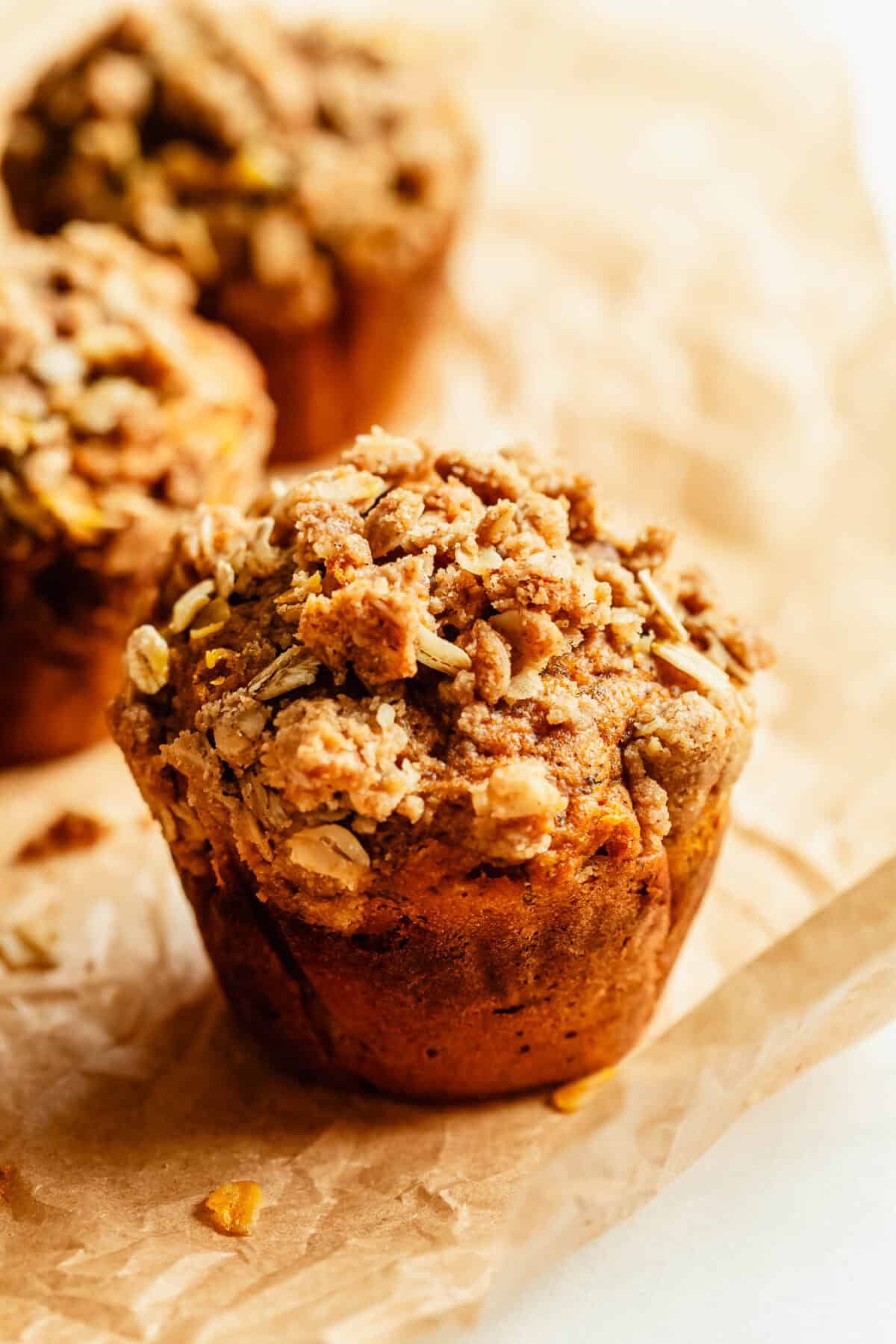 Two banana pumpkin muffins with crumble topping on parchment paper.