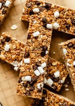 Close-up of chewy s'mores granola bars piled on parchment paper, showing chocolate chunks and mini marshmallows.