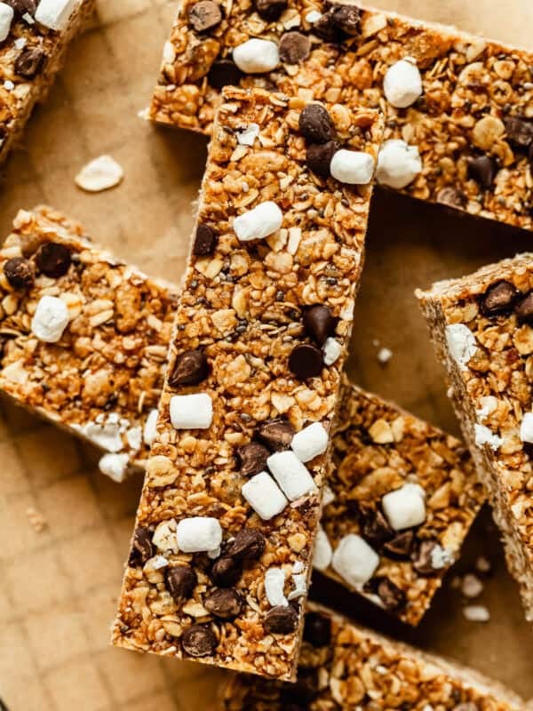 Close-up of chewy s'mores granola bars piled on parchment paper, showing chocolate chunks and mini marshmallows.