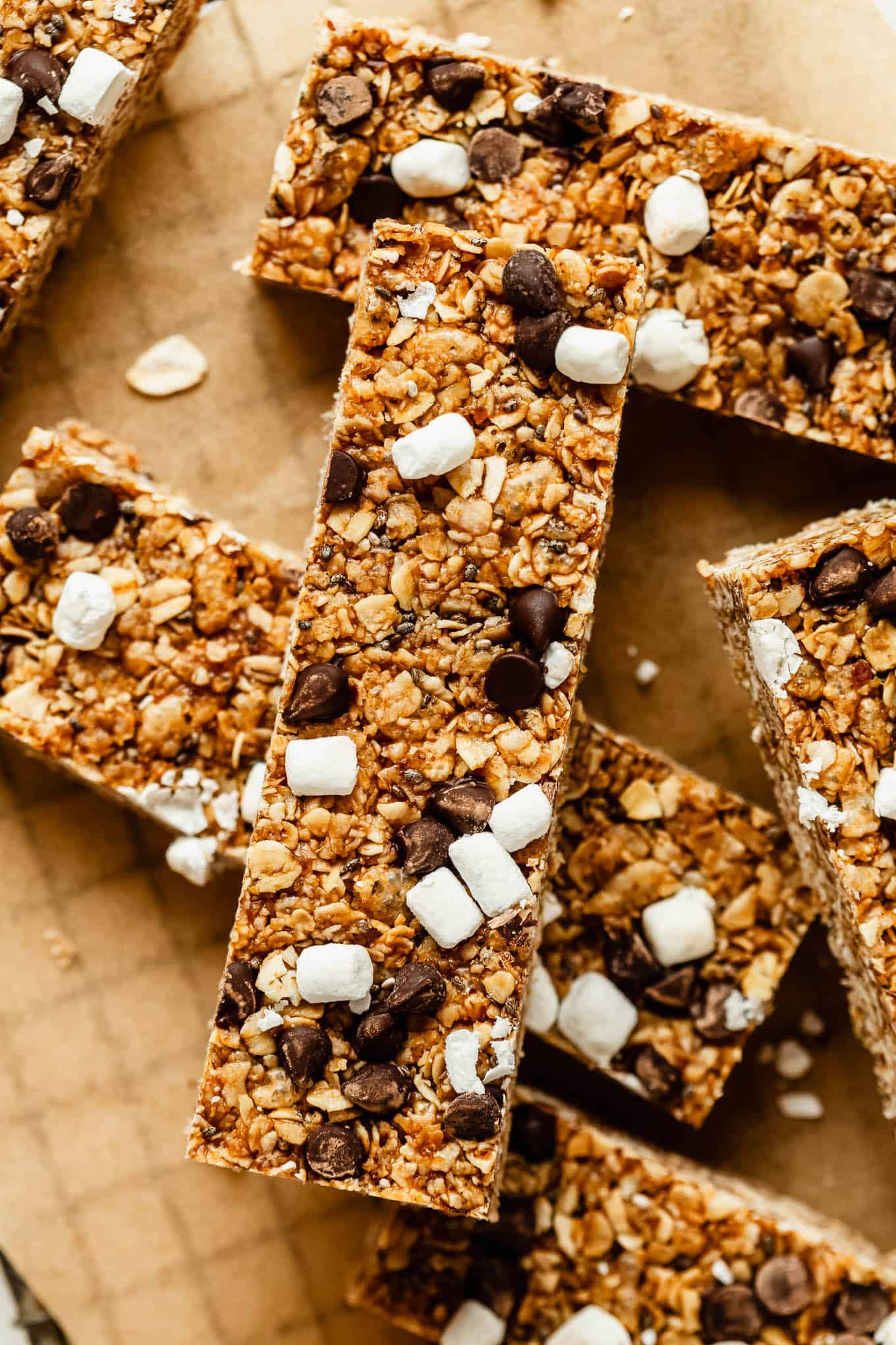 Close-up of chewy s'mores granola bars piled on parchment paper, showing chocolate chunks and mini marshmallows.