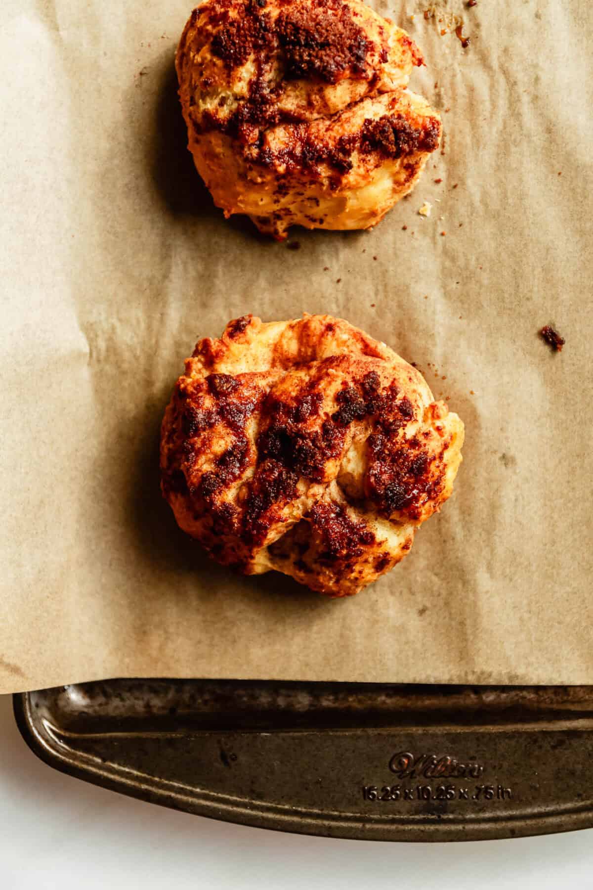 Overhead view of two golden cottage cheese cinnamon crunch biscuits on parchment paper.