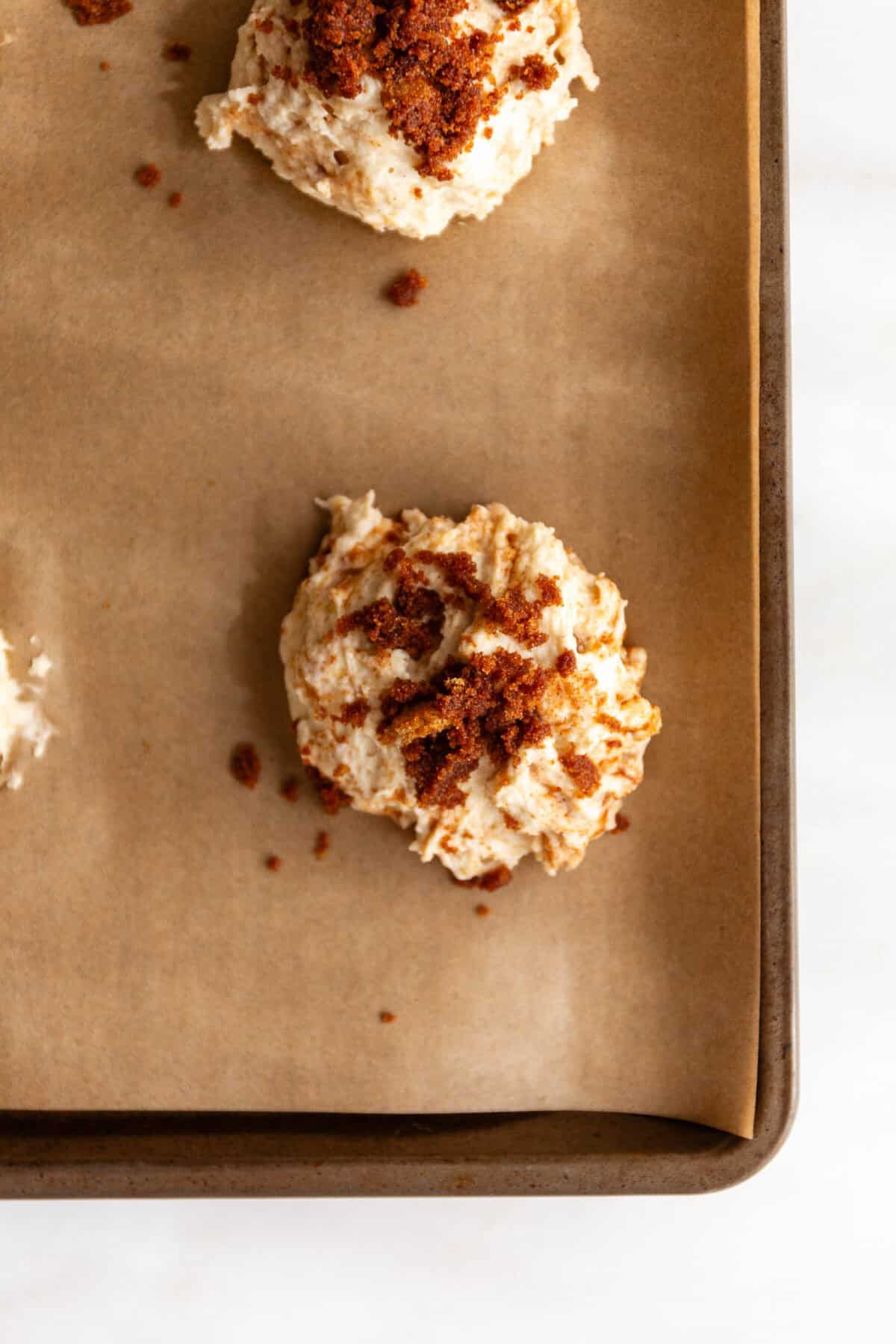 Unbaked cottage cheese cinnamon crunch biscuit dough mounds topped with cinnamon sugar crumble on a parchment-lined baking sheet