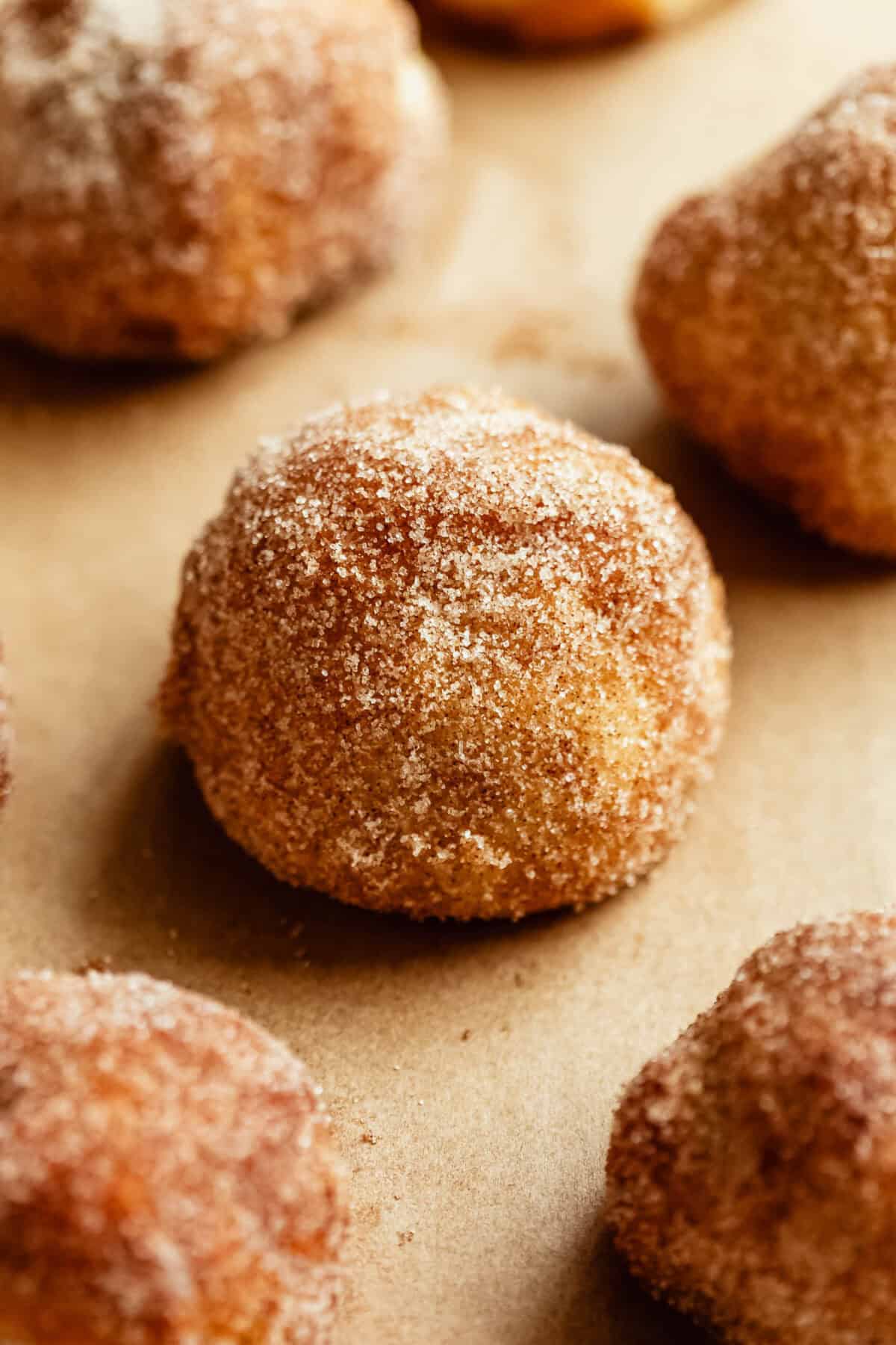 A close-up of golden donut holes coated in cinnamon sugar on parchment paper.