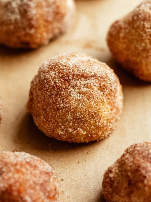 A close-up of golden donut holes coated in cinnamon sugar on parchment paper.