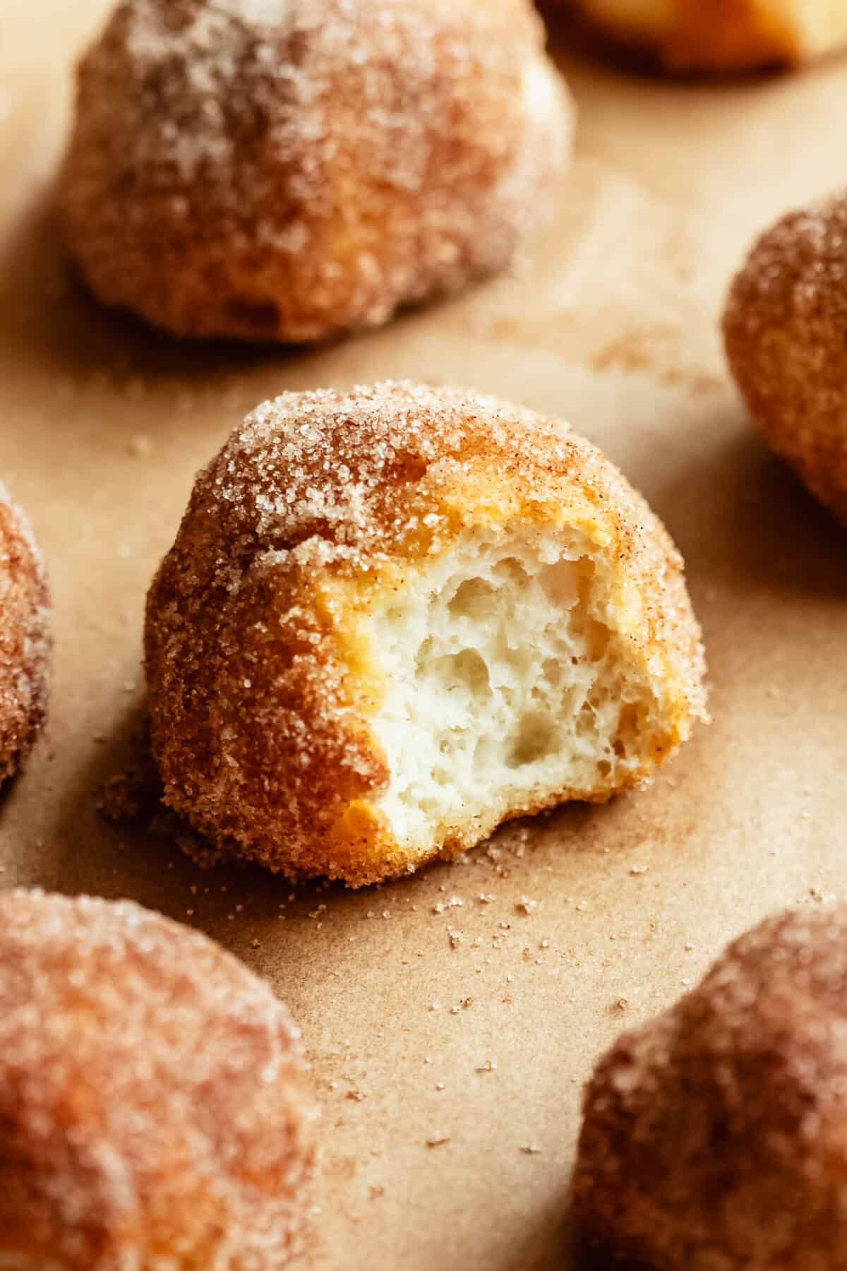 A cinnamon sugar donut hole torn open to reveal its soft, fluffy interior, surrounded by more donut holes.