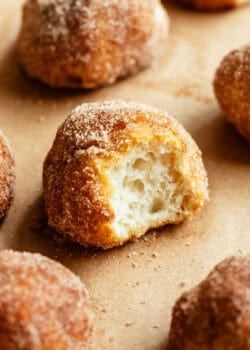 A cinnamon sugar donut hole torn open to reveal its soft, fluffy interior, surrounded by more donut holes.