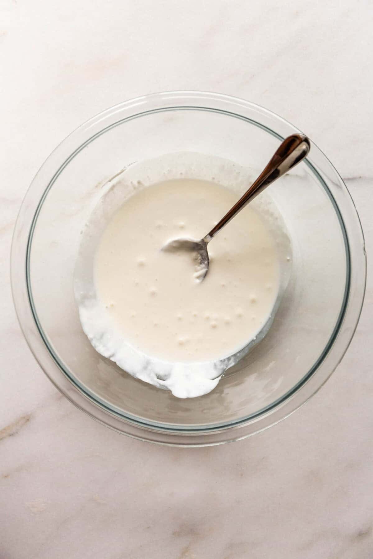 A glass bowl of smooth, creamy batter with a spoon resting inside.