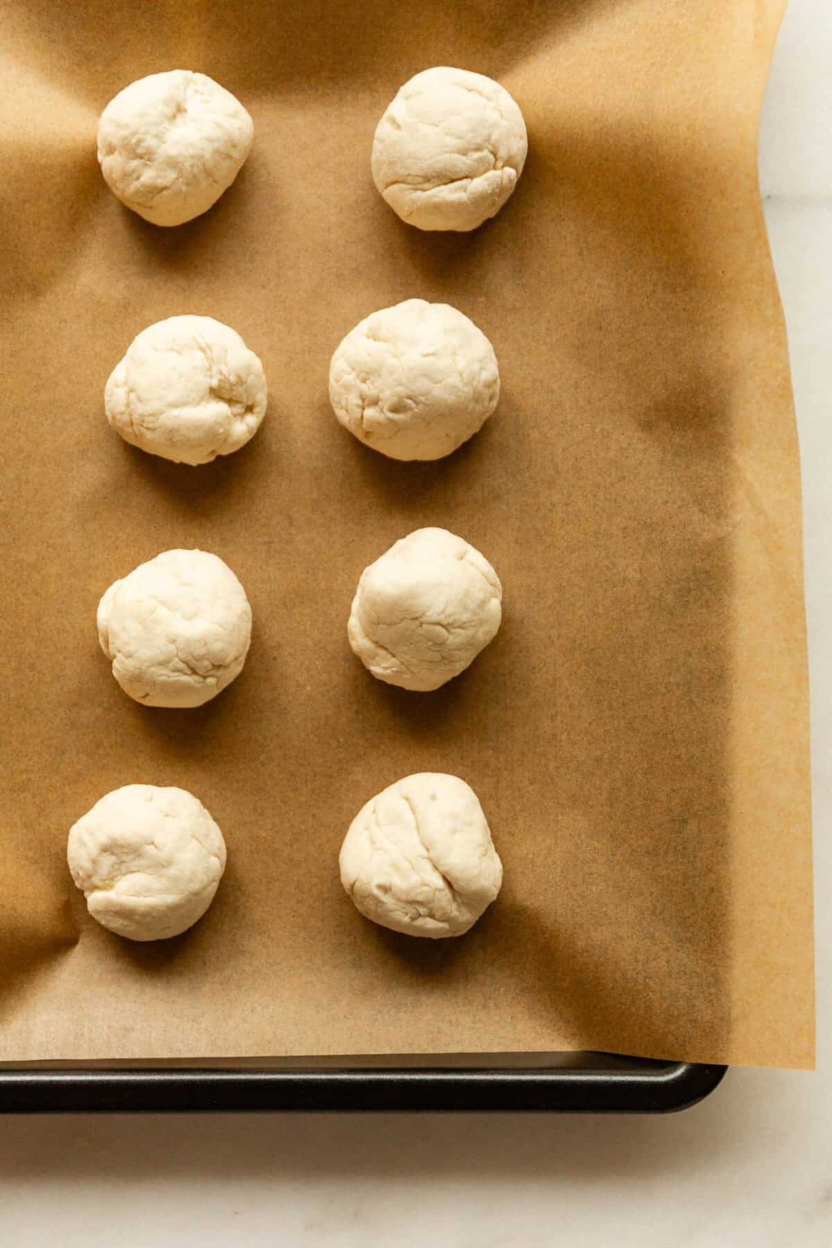 Rows of round dough balls arranged on a parchment-lined baking sheet before baking.