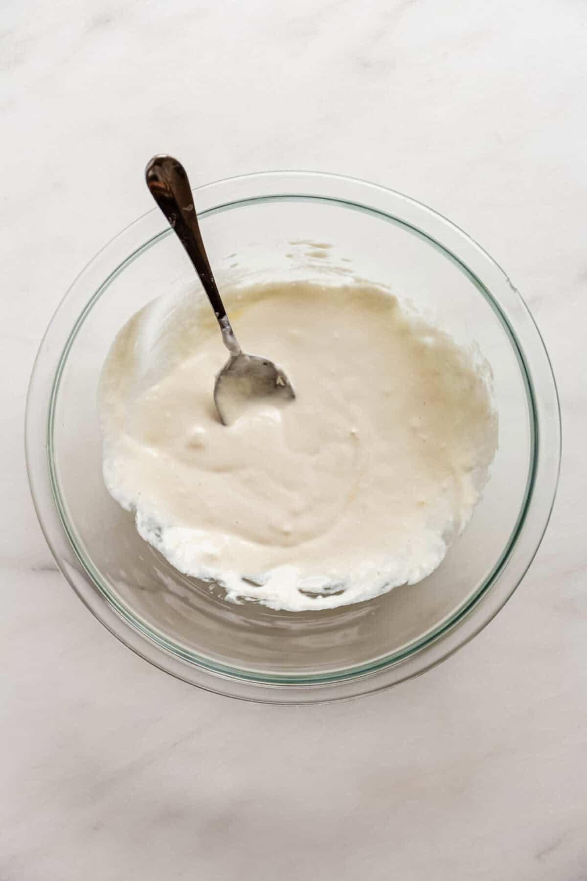 Bowl of smooth cottage cheese batter for apple fritters with a spoon.