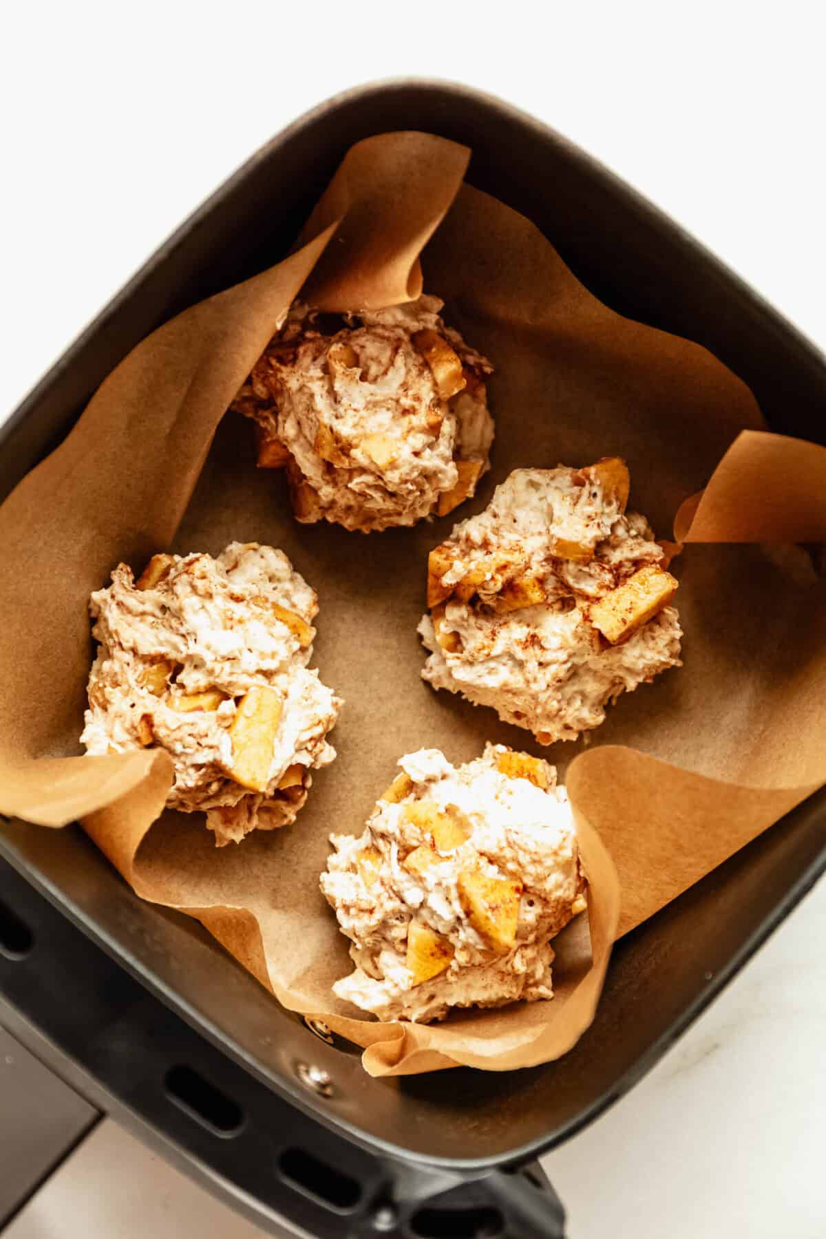 Scoops of cottage cheese apple fritter batter in an air fryer basket before cooking.