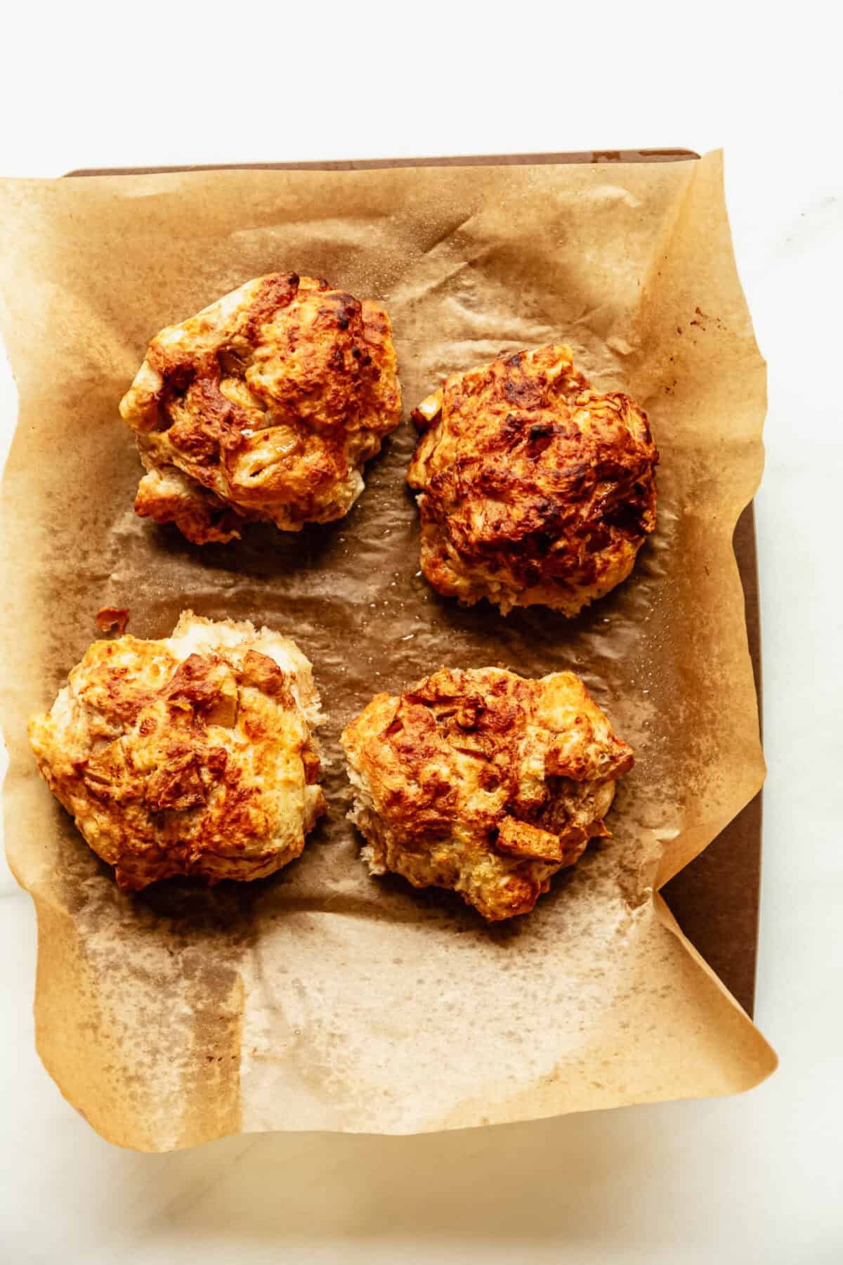 Four golden cottage cheese apple fritters fresh out of the air fryer on parchment paper.