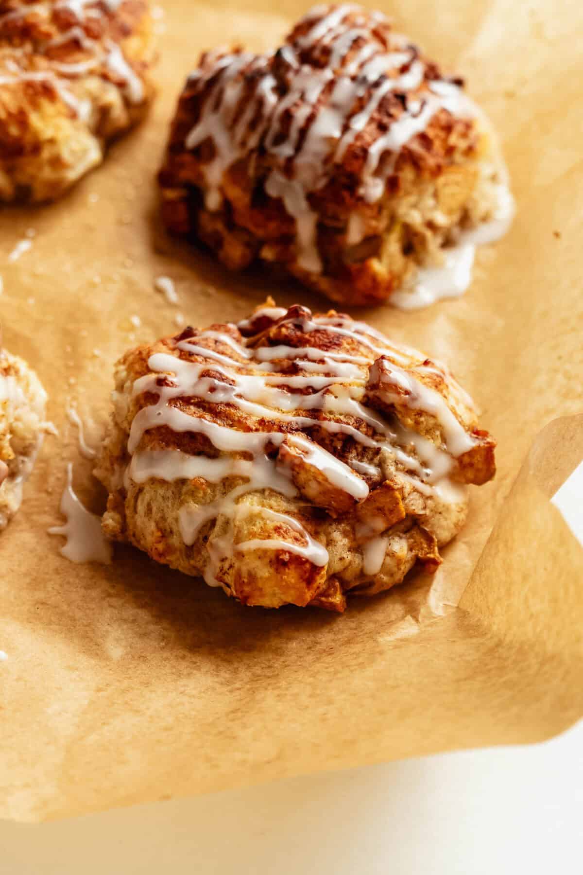 Cottage cheese apple fritters drizzled with a sweet glaze on parchment paper.