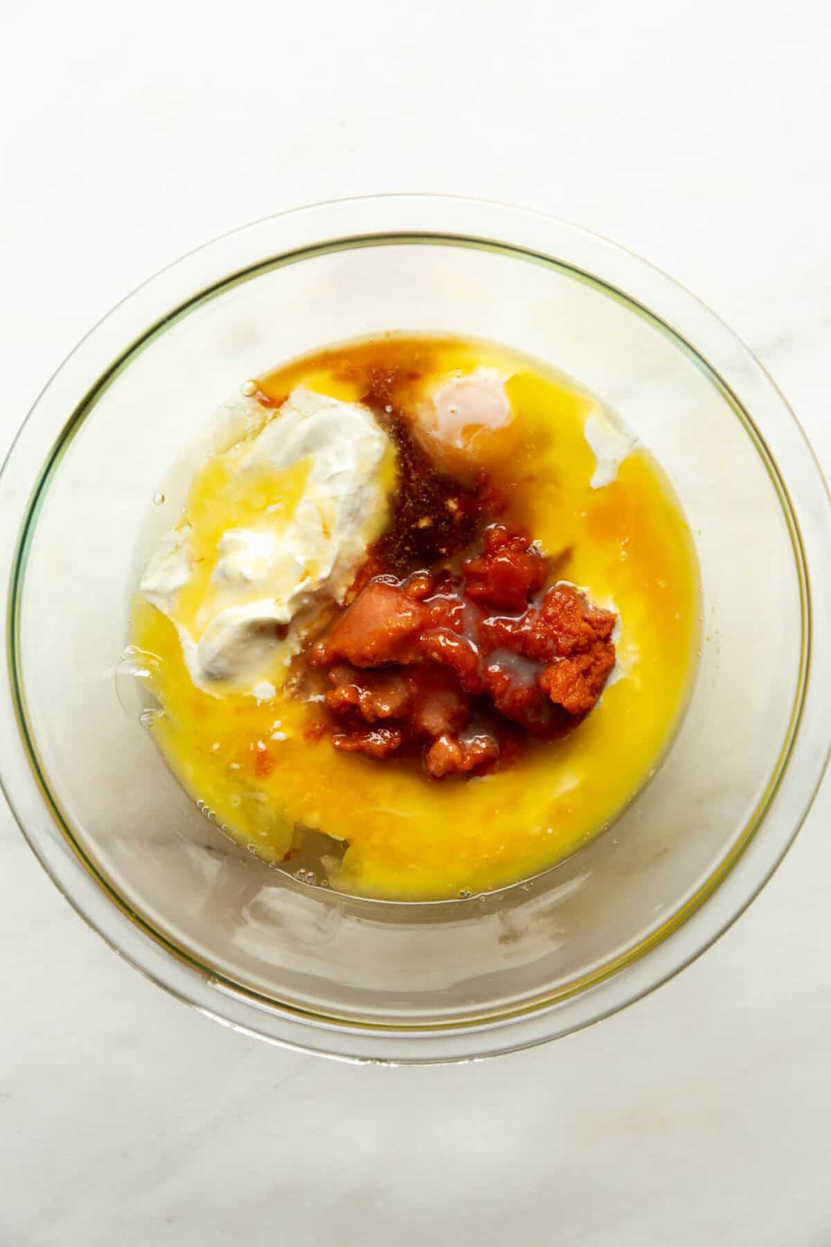 Wet ingredients for cottage cheese pumpkin muffins, including eggs, cottage cheese, melted butter, and pumpkin puree, in a glass mixing bowl.