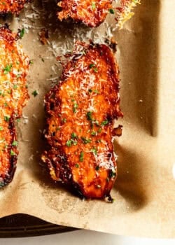 A single parmesan roasted sweet potato wedge topped with parsley, served in parchment paper.