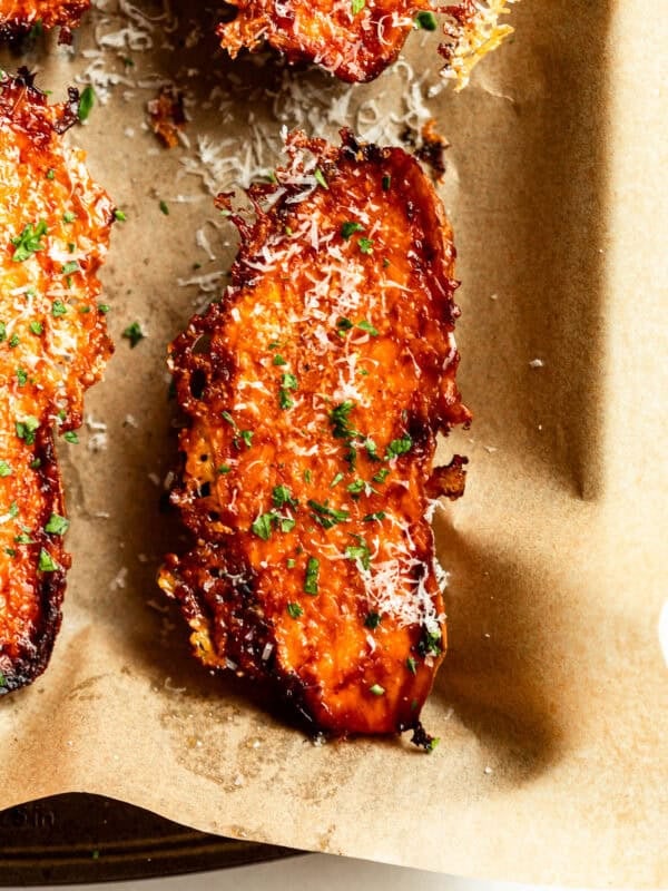 A single parmesan roasted sweet potato wedge topped with parsley, served in parchment paper.