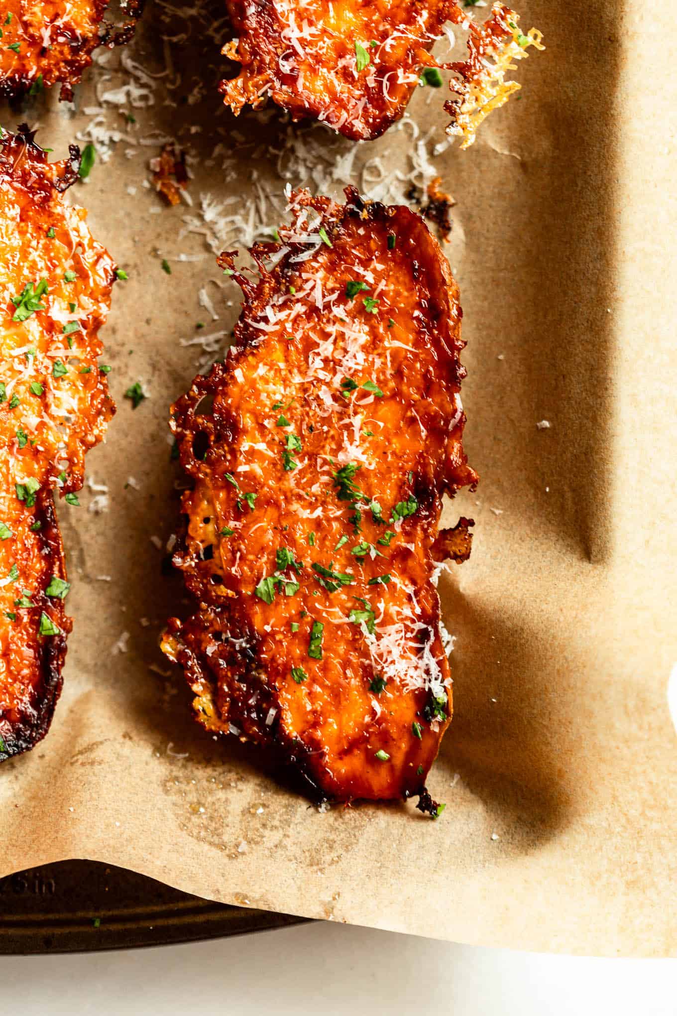 A single parmesan roasted sweet potato wedge topped with parsley, served in parchment paper.