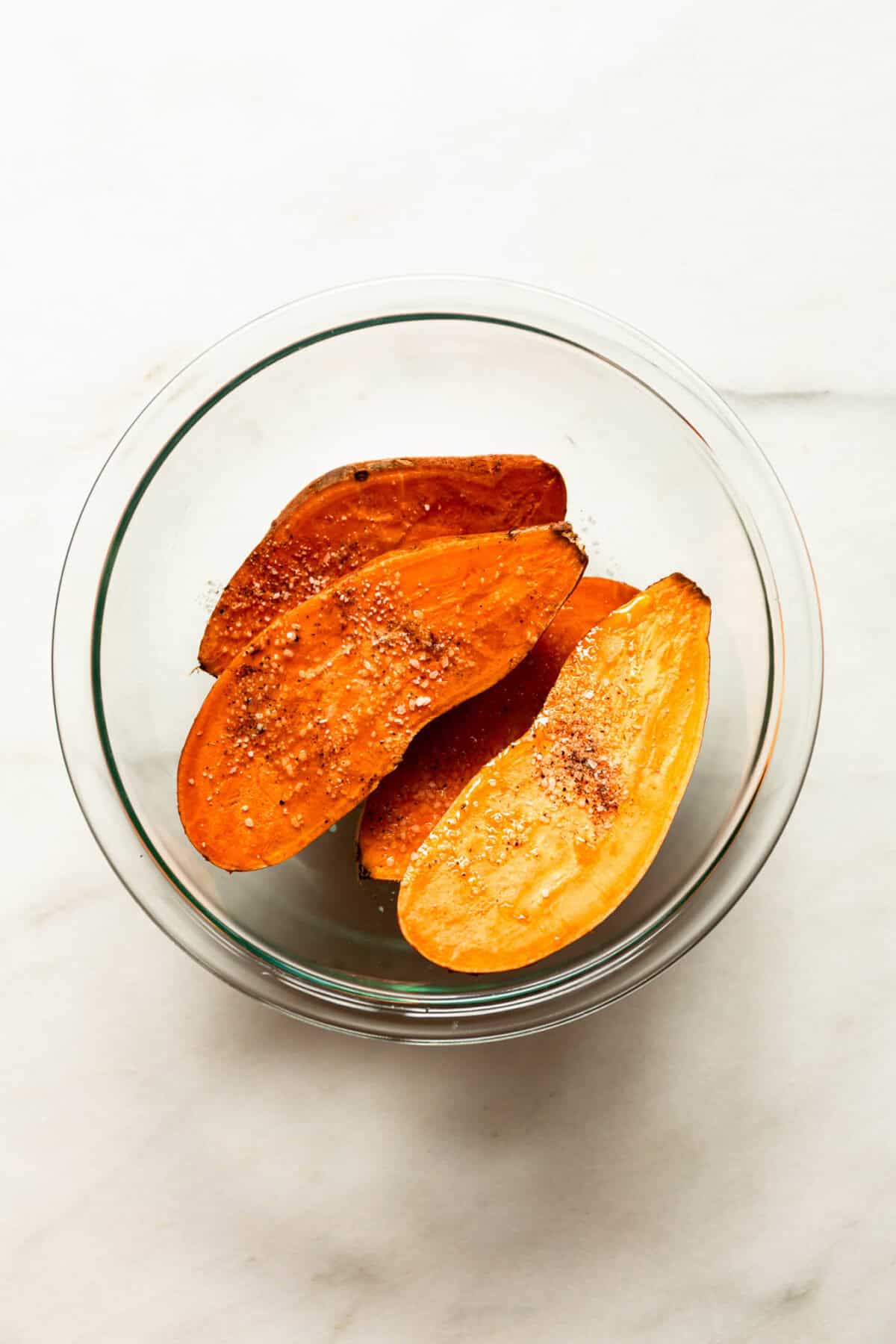 Sliced parmesan roasted sweet potato wedges in a glass bowl on a marble countertop.