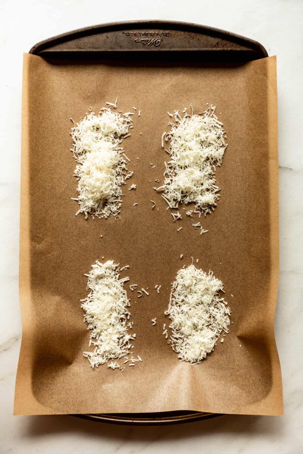 Sweet potato slices topped with shredded parmesan cheese on a parchment-lined baking sheet, ready to roast.