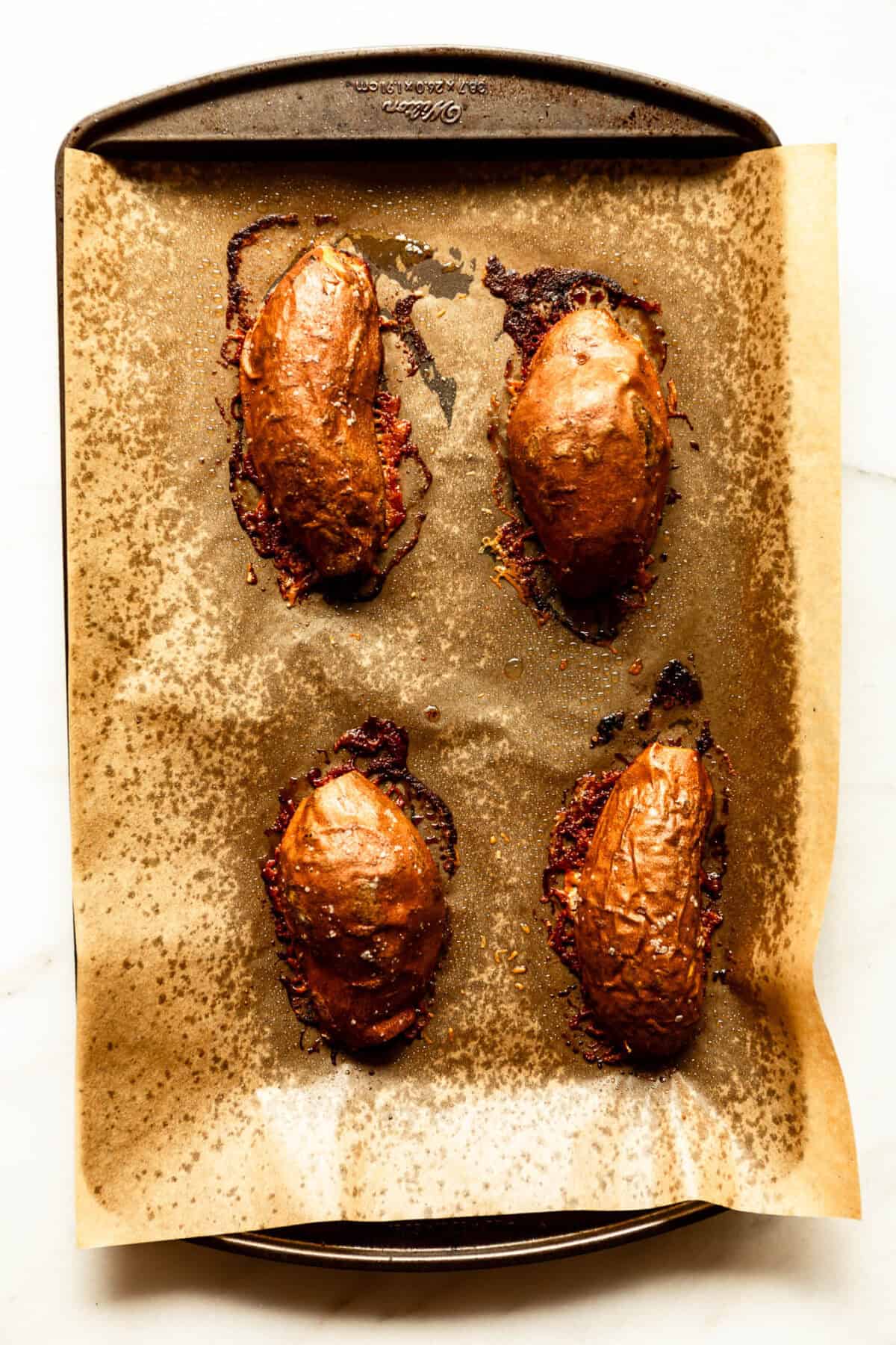 Roasted parmesan sweet potato halves with a golden, crispy cheese crust on a baking sheet.
