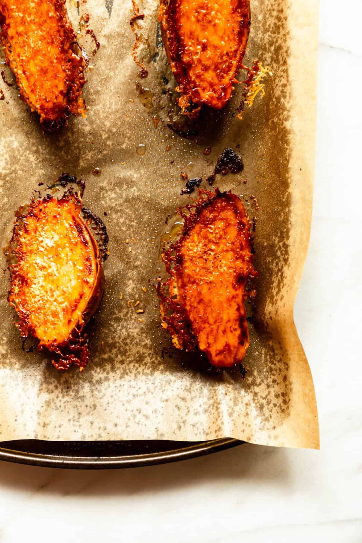 Close-up of crispy parmesan roasted sweet potato slices on a baking sheet.