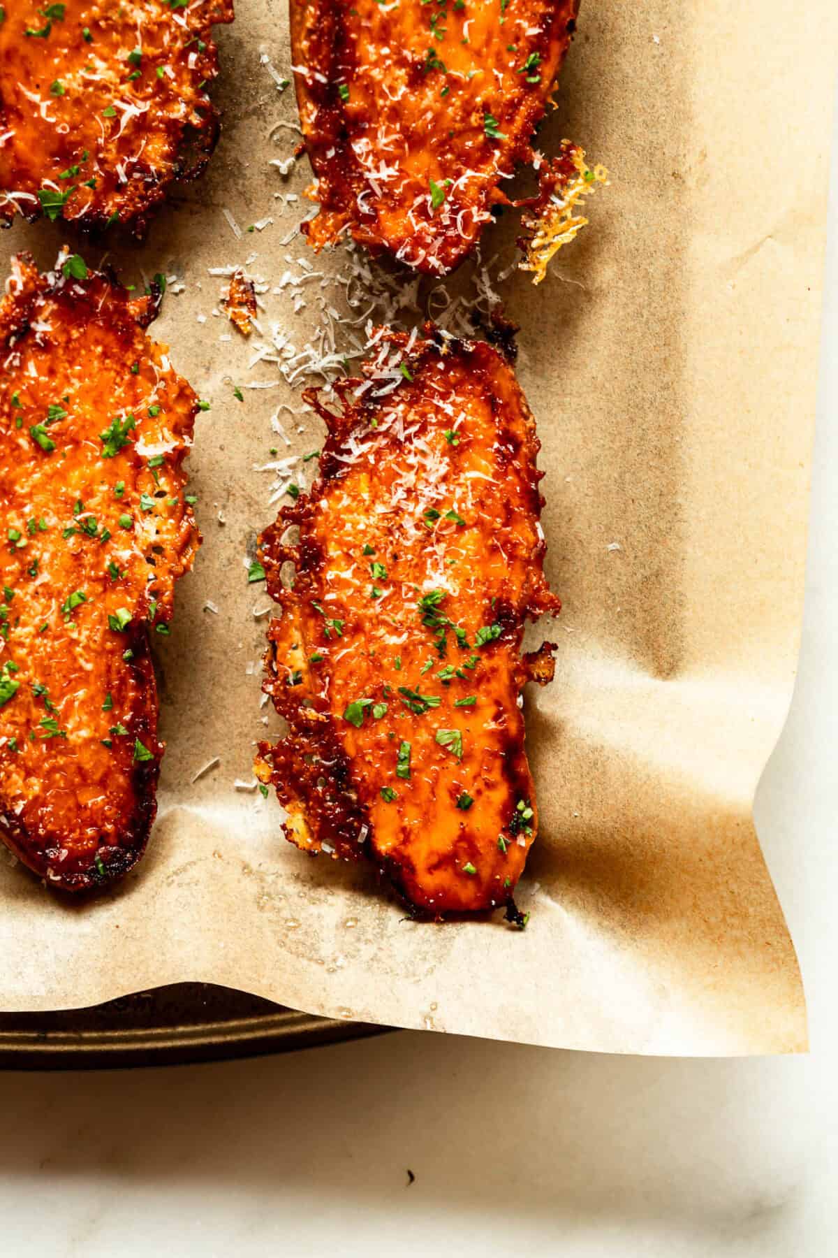 Roasted parmesan sweet potato wedges garnished with fresh parsley on parchment paper.