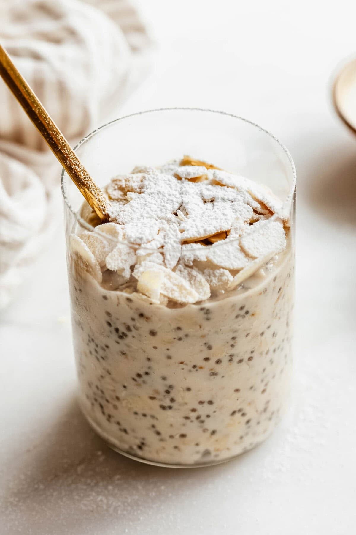 Close-up of almond croissant overnight oats in a glass topped with toasted sliced almonds and a dusting of powdered sugar.