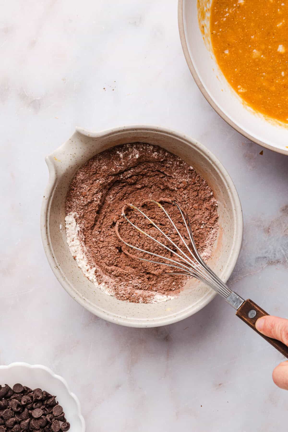 Whisking cocoa powder and dry ingredients in a bowl next to mashed banana for banana brownies