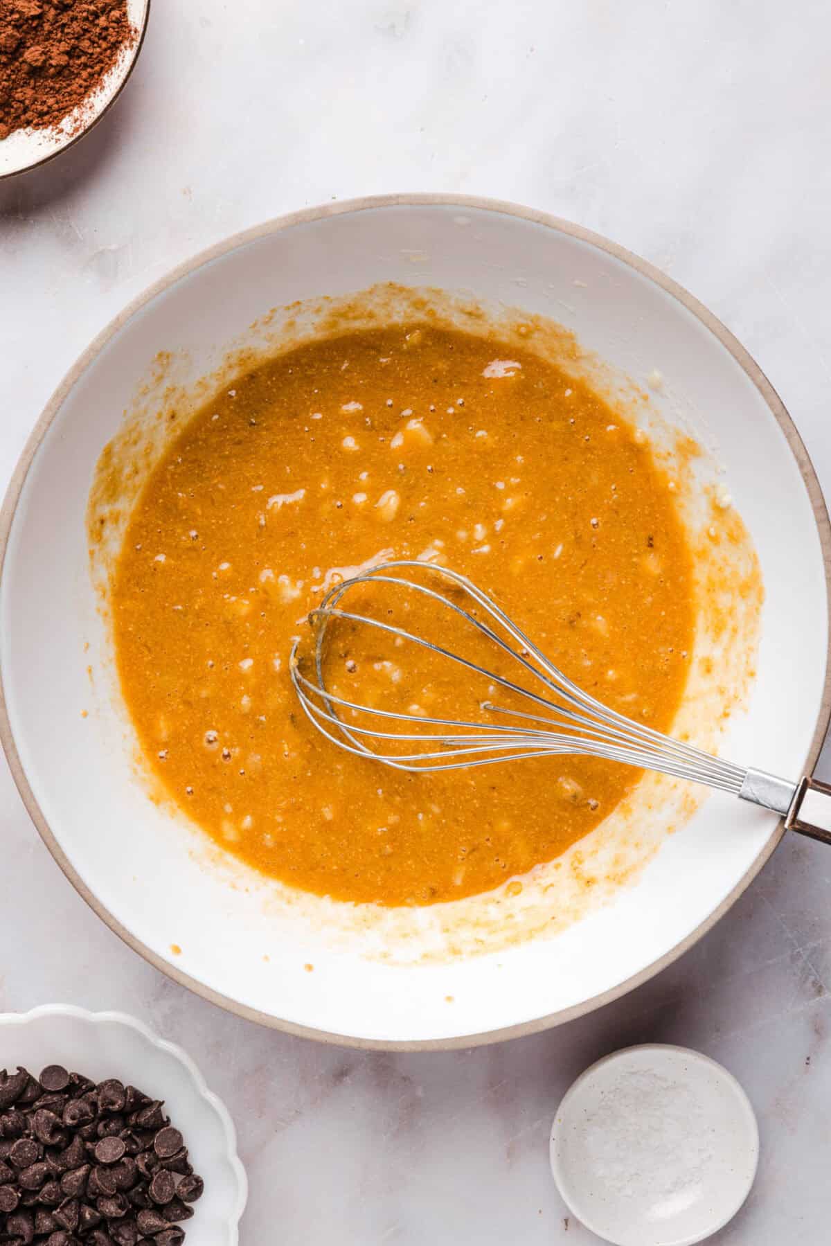 a white bowl with mixed egg, mashed banana and peanut butter with a whisk in it.