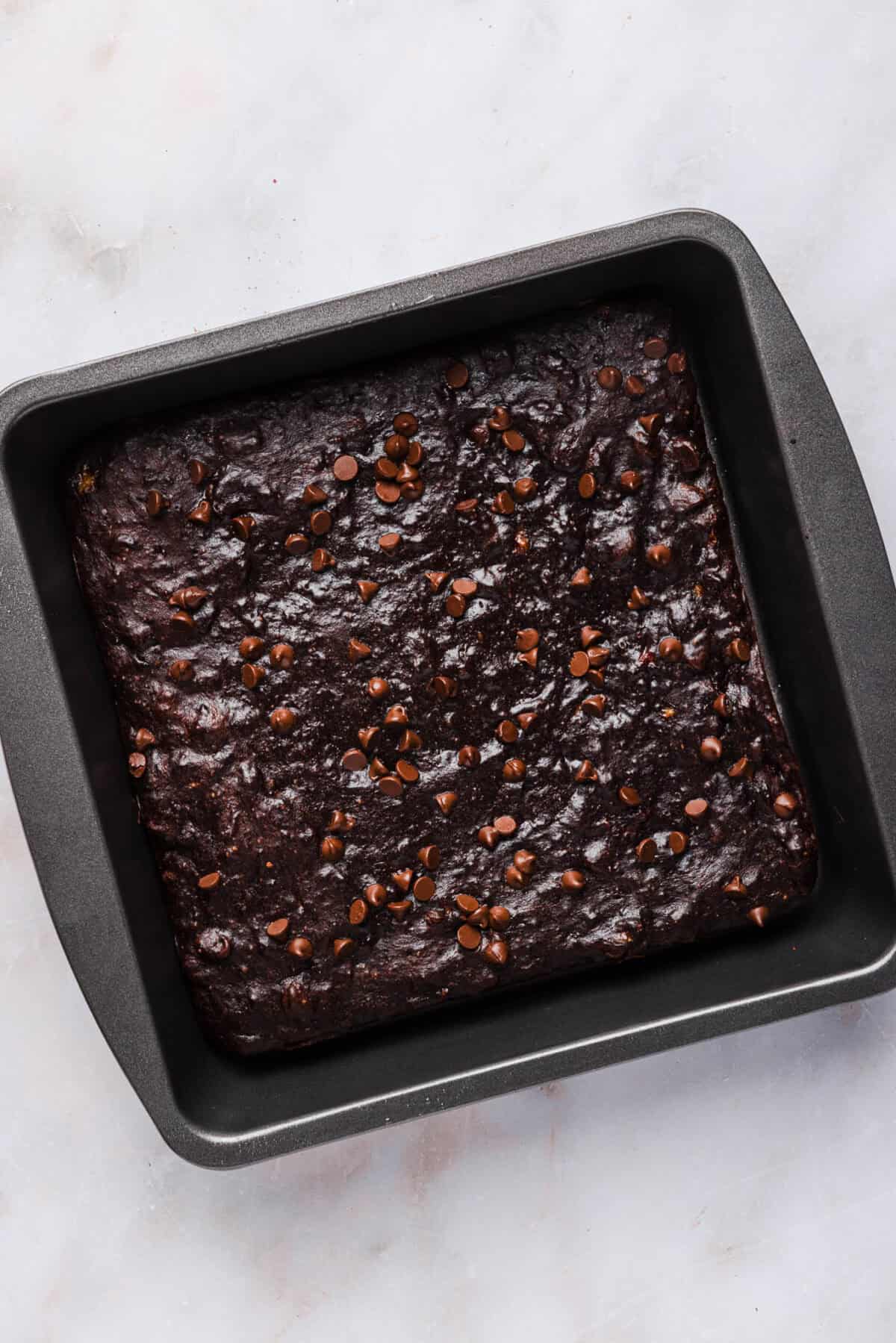 Baked banana brownies cooling in a square pan with a crackly chocolate top