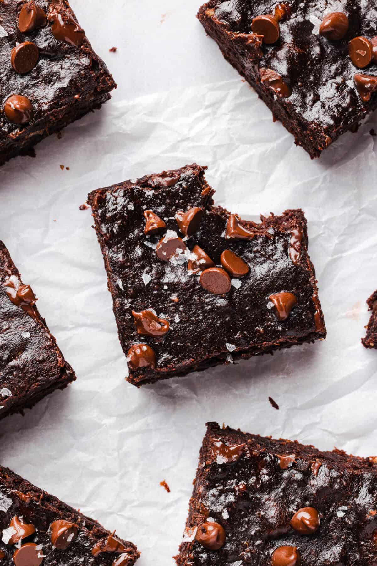 Banana brownies cut into squares and scattered on parchment paper, topped with melty chocolate chips