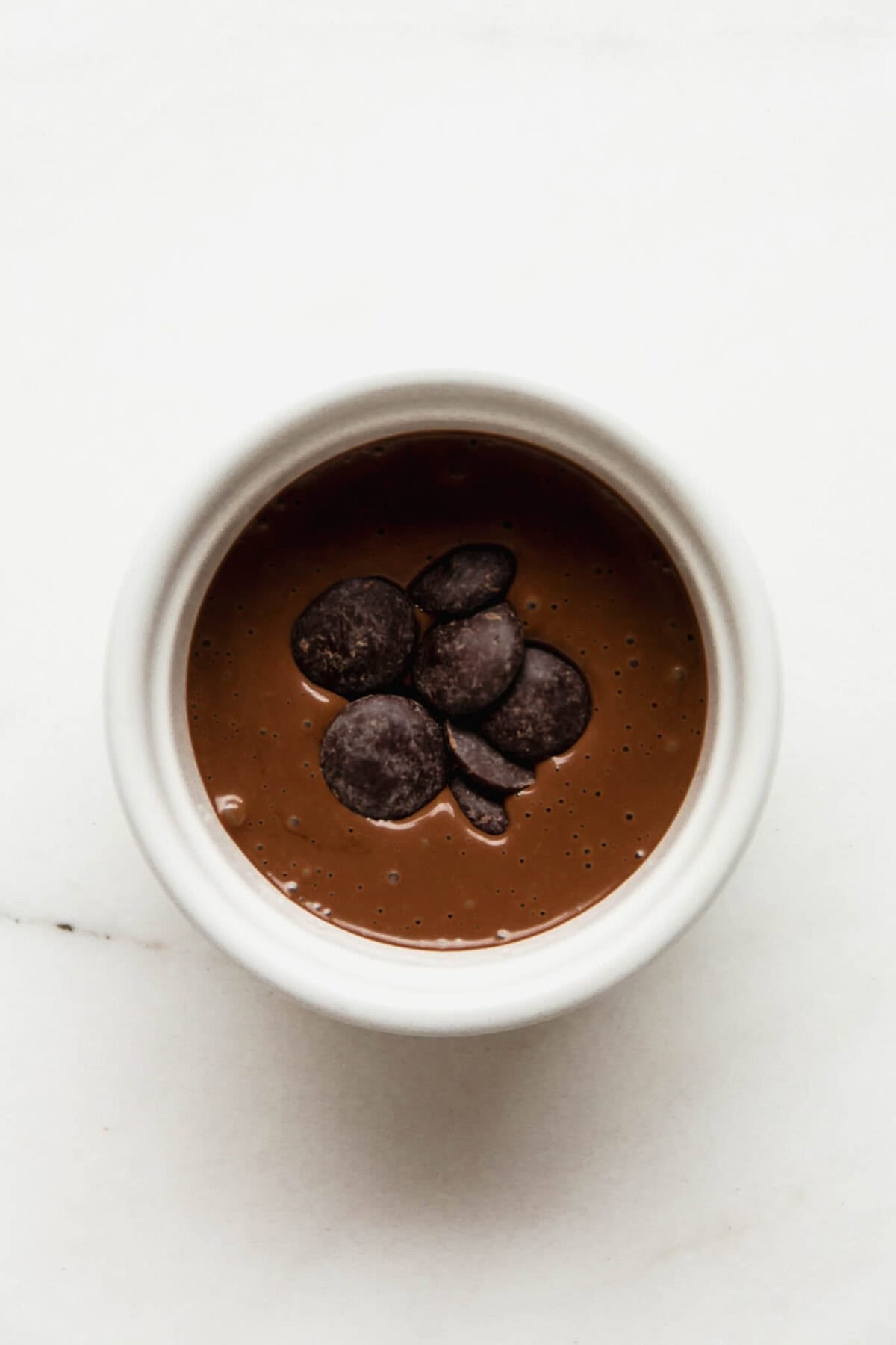 Dark chocolate wafers pressed into the center of chocolate batter in a white ramekin before baking.