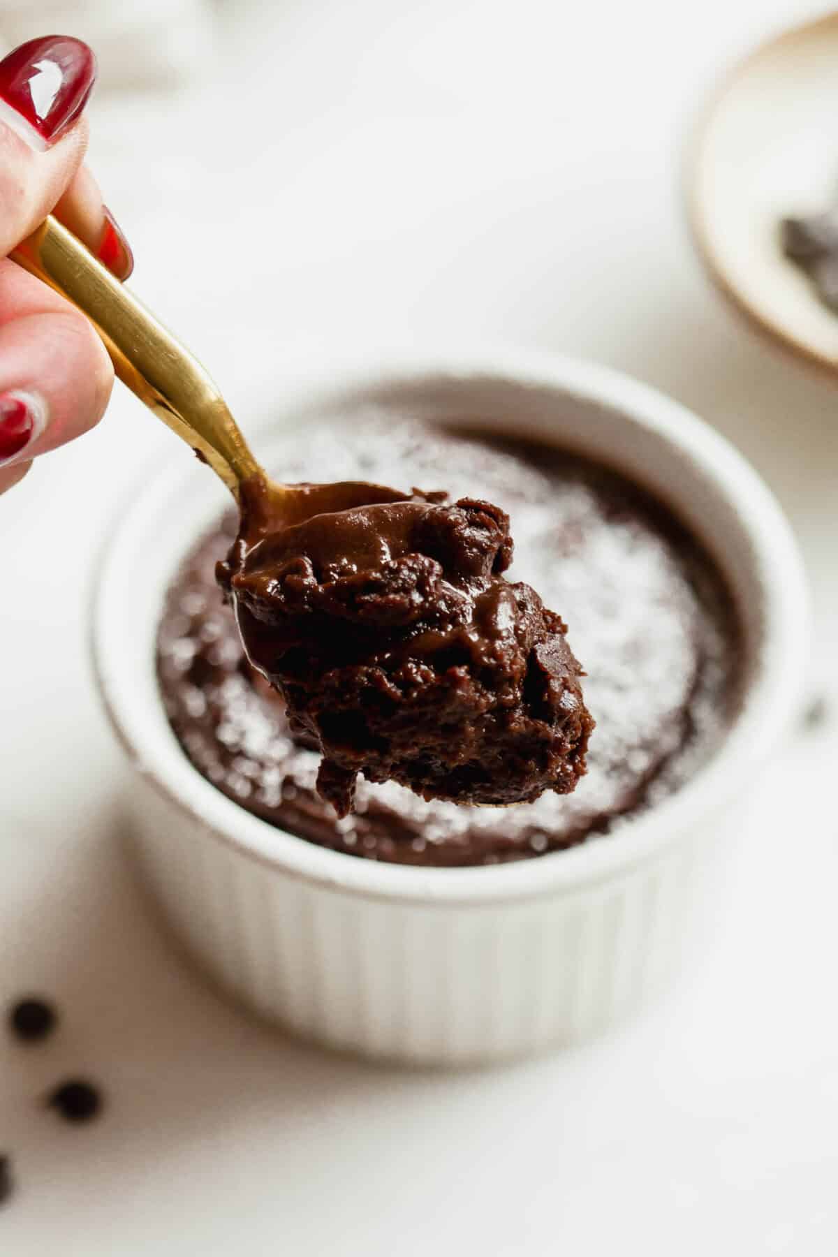Gold spoon lifting a scoop of gooey molten chocolate from a cottage cheese chocolate lava cake in a white ramekin.