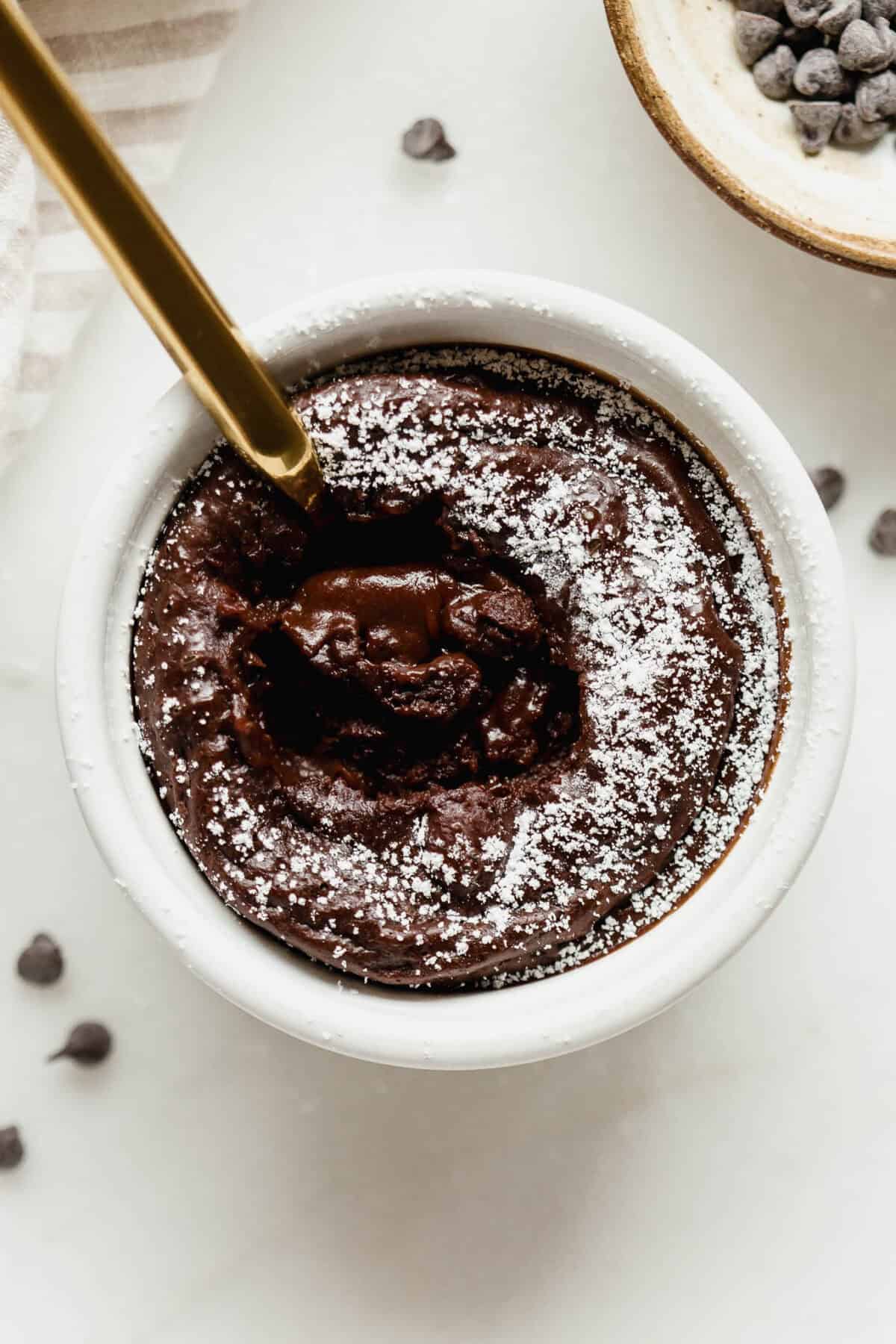 Close-up of a gold spoon in a cottage cheese chocolate lava cake with a gooey melted chocolate center and powdered sugar on top.