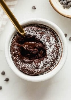 Close-up of a gold spoon in a cottage cheese chocolate lava cake with a gooey melted chocolate center and powdered sugar on top.