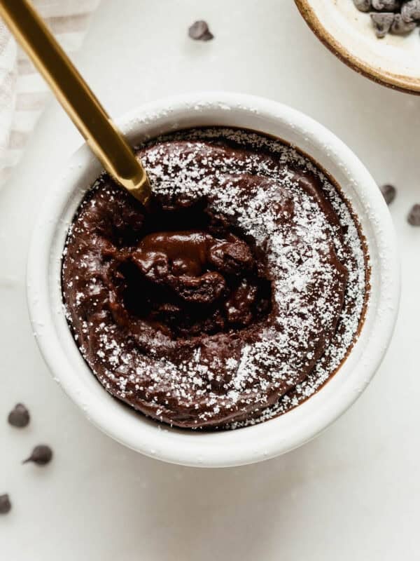 Close-up of a gold spoon in a cottage cheese chocolate lava cake with a gooey melted chocolate center and powdered sugar on top.