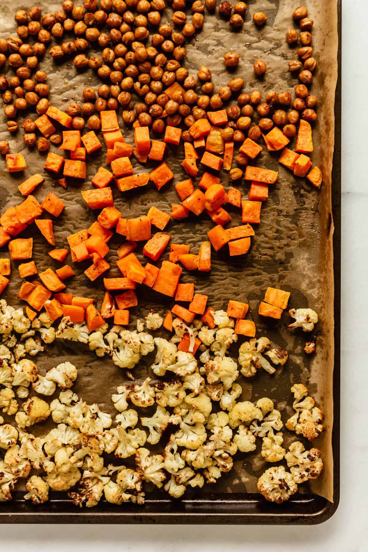 Roasted chickpeas, sweet potatoes, and cauliflower on baking sheet for healthy snack.