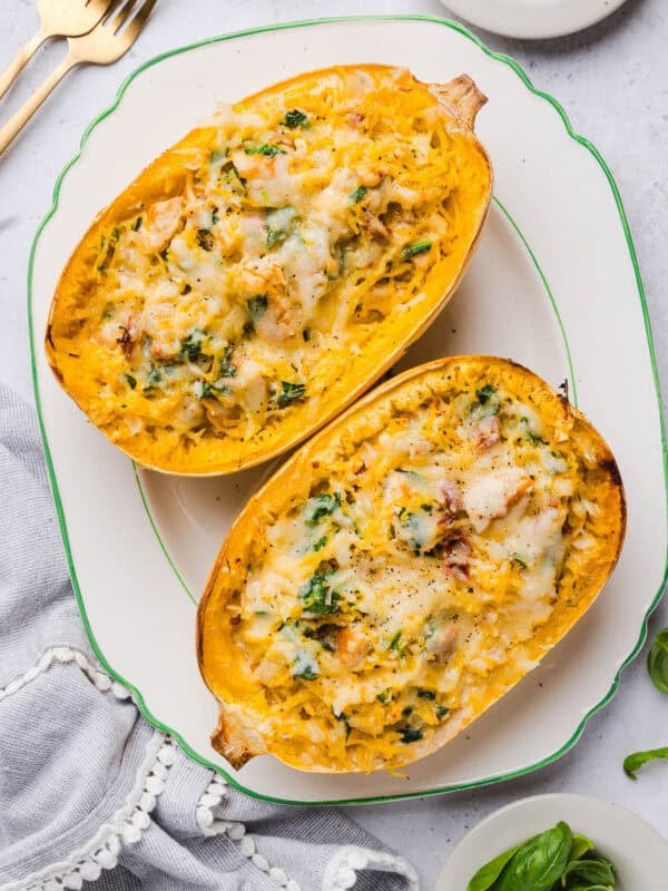 Two halves of marry me spaghetti squash with chicken and spinach served on a white platter