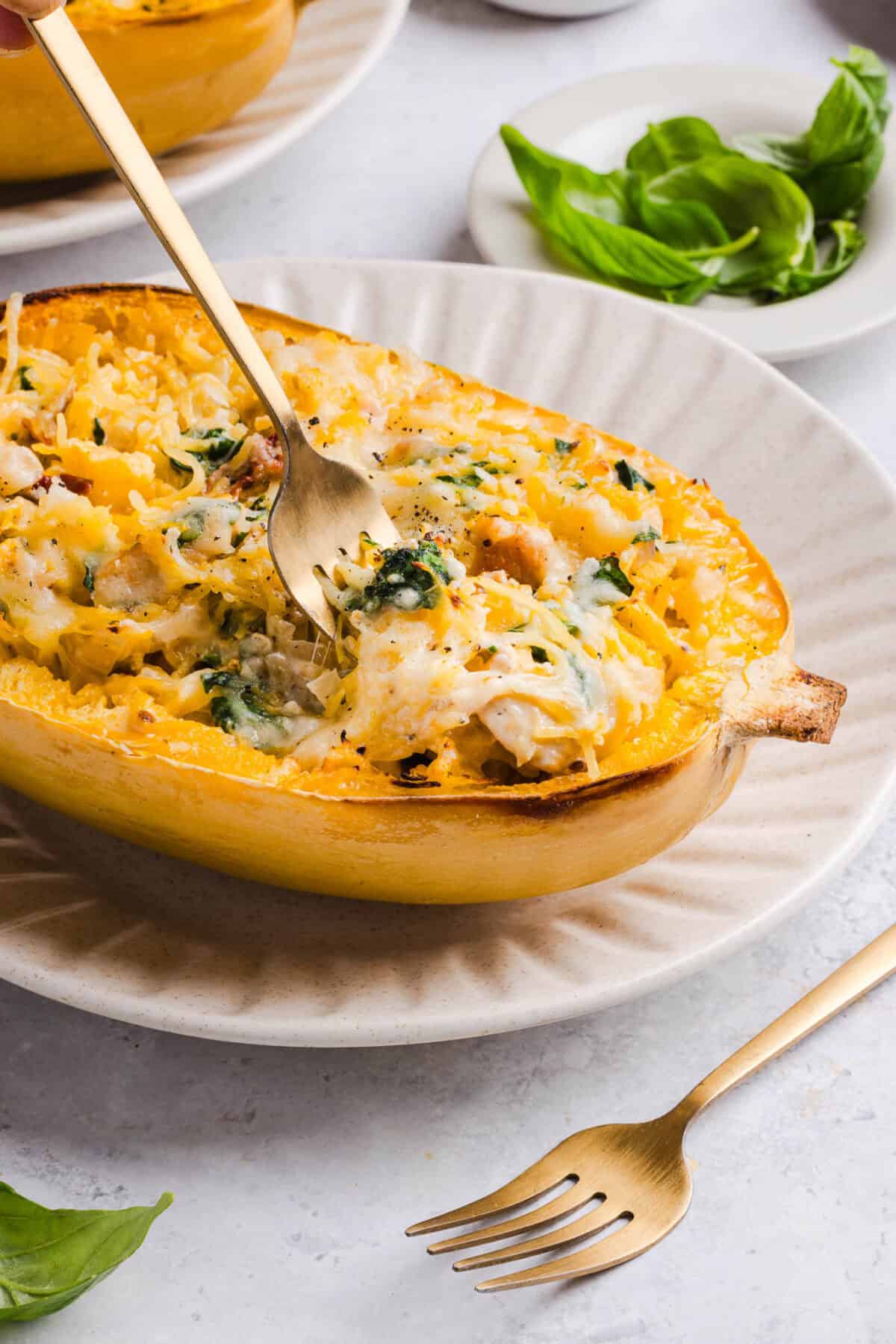 Fork twirling into a cheesy marry me spaghetti squash boat on a plate, with fresh basil on the side
