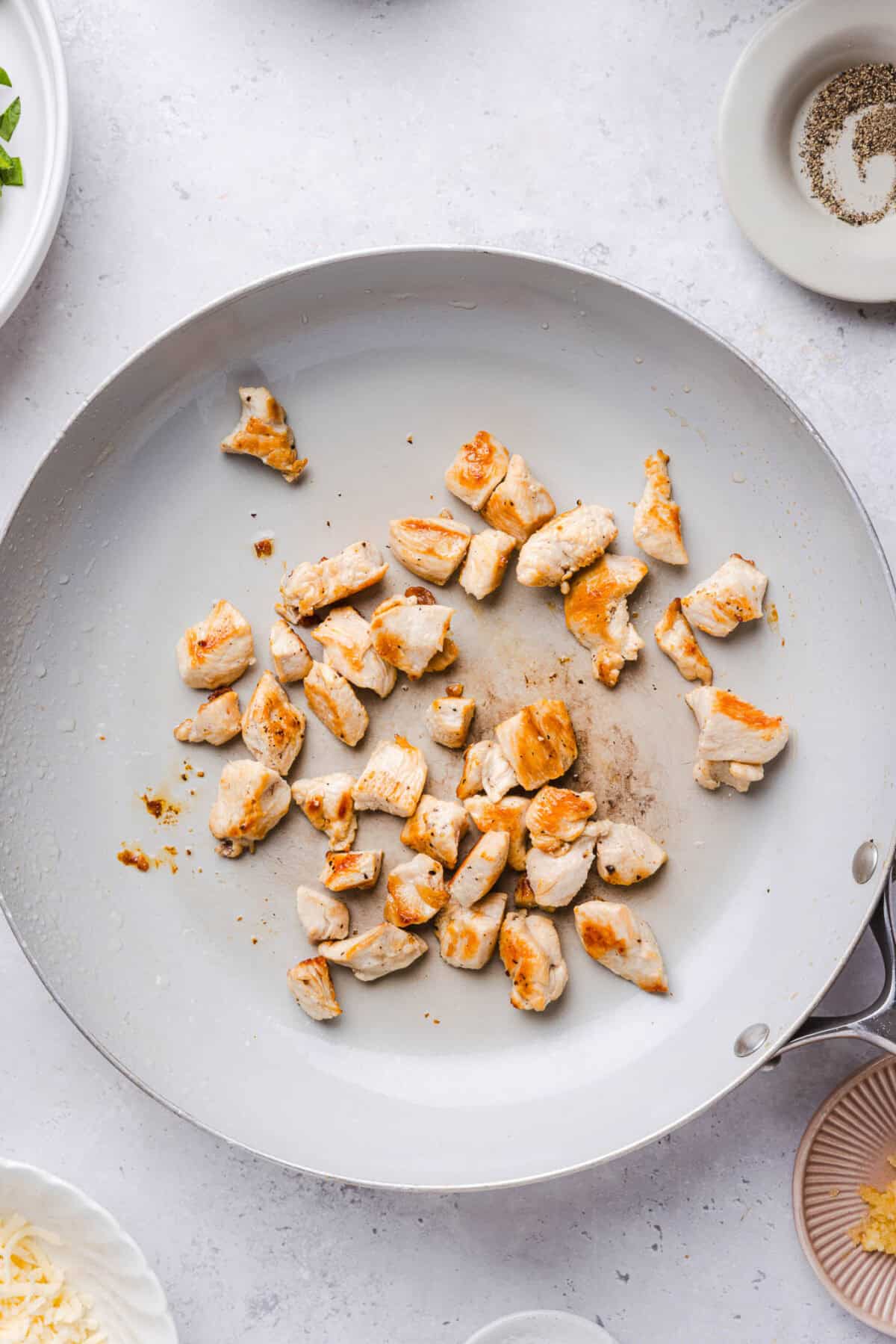 Bite-sized pieces of chicken browning in a white skillet